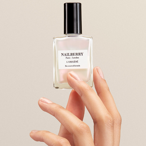 Nailberry nail polish bottle held by a hand with pink nails against a beige background