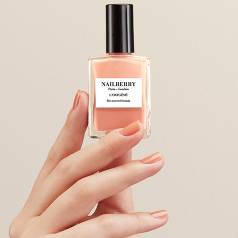 Hand holding a Nailberry nail polish bottle with a beige background