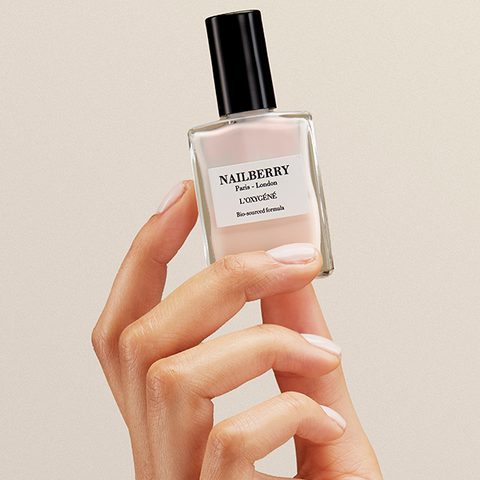Hand holding a Nailberry nail polish bottle against a beige background